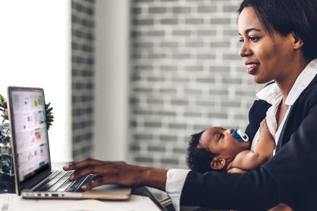 Portrait of black mother relaxing using technology of laptop computer with black baby while sitting on table. Young creative african woman working at home. work from home concept